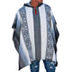 Person wearing a striped poncho with geometric patterns stands casually against a plain white background. The garment drapes over their shoulders, while they wear ripped blue jeans underneath.