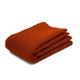 A folded, reddish-orange blanket lies neatly against a plain white background, emphasizing its color and texture.
