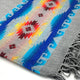 A woven rug displays intricate geometric patterns in red, yellow, and blue on a gray base. Fringe edges adorn the sides, enhancing the textile's decorative appeal.
