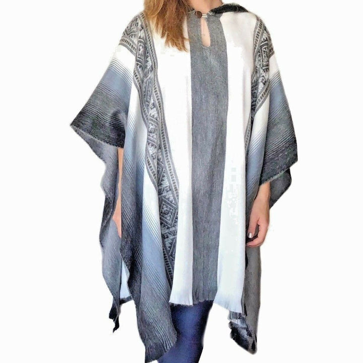 Poncho worn by a person; the poncho features vertical black, white, and gray stripes with intricate patterns. The person is standing against a plain white background.