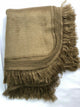 A folded brown blanket with decorative fringe trim is neatly placed on a flat, white surface. The blanket features intricate woven patterns near the edges.