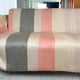 Tilivi baby alpaca wool blanket – a sofa covered with a fabric displaying vertical stripes in shades of beige, gray, and pink stands on a carpeted floor with a subtle zigzag pattern
