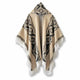 A poncho with geometric black patterns and fringed edges hangs against a white background, displaying a central hood and patterned borders.