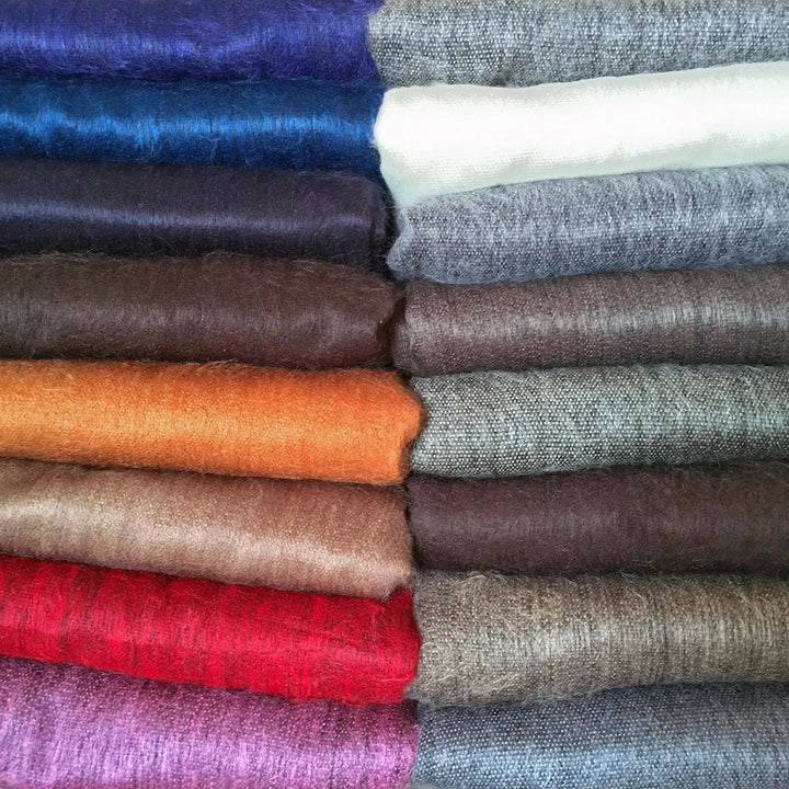 Apatug baby alpaca wool blanket – stacked colorful wool fabrics, including blue, white, gray, orange, and red shades, are neatly arranged in two vertical columns, highlighting texture and color variety in a textile shop setting