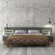 Bed with geometric-patterned blanket has two white pillows, flanked by gray nightstands. Two pendant lights hang above, set against a textured gray wall and wooden floor.