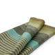 Cojitambo alpaca wool throw blanket – a folded fabric with alternating stripes in muted greens, grays, blues, and browns lies on a white surface, emphasizing its soft texture and elegant design