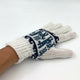 A white knitted glove, adorned with dark blue geometric patterns, is worn on a hand resting against a plain, light background.