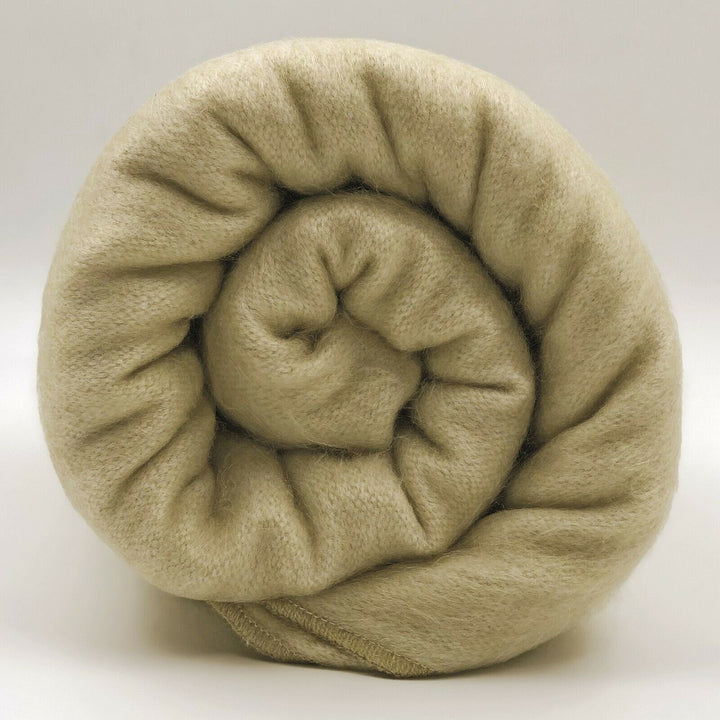 Llullalo baby alpaca wool blanket – a rolled-up beige blanket sits in close-up view against a plain white background, showcasing its soft, textured surface