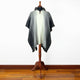 Zuleta llama wool hooded poncho – a gray gradient poncho is displayed on a wooden mannequin stand, featuring a hood and button detail, set against a plain white wall and wooden floor
