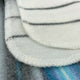Teinza baby alpaca wool blanket – white fabric pads are stacked, featuring black horizontal lines, positioned on a blue and gray striped surface. The pads have visible stitching along their edges