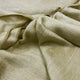 Llullalo baby alpaca wool blanket – a close-up of a beige, textured fabric with soft, visible folds and neat edging, laying flat. The warmth and wool-like appearance suggest comfort and coziness