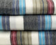 Carihuairazo baby alpaca wool blanket – stacked wool blankets with colorful stripes in blue, gray, and pink rest neatly, creating a cozy and textured visual pattern against a plain background
