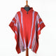 Red poncho is displayed on a wooden mannequin, featuring purple and white vertical stripes. The setting is a plain white background, enhancing the garment's vibrant colors.