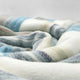 Chuquipogyo baby alpaca wool blanket – a soft, multi-colored woolen fabric rests in gentle folds, displaying stripes of blue, gray, and cream against a neutral, blurred background
