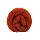 A rolled, textured, red-orange fabric, possibly a blanket or scarf, positioned upright against a plain white background.