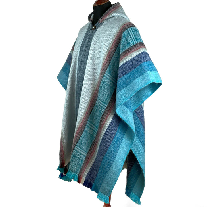 A mannequin displays a blue and teal striped poncho with intricate patterns. The poncho drapes smoothly, showing diverse textures and hues in a simple, white background.