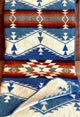 A wool blanket with geometric patterns in blue, white, brown, and red rests on a surface. The design features triangles and zigzags, creating a southwestern aesthetic.