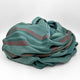 Pallalanga baby alpaca wool blanket – a folded, teal-colored cloth with reddish-brown stripes lies crumpled on a plain white surface, giving a sense of casual, elegant texture