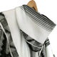 A woven, white and gray striped fabric drapes over a wooden hanger, showcasing intricate patterns in a close-up view.