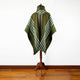 A green and white striped poncho with a brown trim is displayed on a wooden stand against a white wall and hardwood floor.
