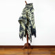 Tarqui alpaca wool hooded poncho – a patterned poncho drapes over a wooden stand. The poncho features geometric shapes with fringe edges. It rests against a white wall on a hardwood floor