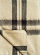 Wholesale lot of 30 queen alpaca wool blankets – a folded woolen blanket, featuring a beige and dark gray plaid pattern, lies on a flat surface. The texture appears soft and slightly fuzzy, suggesting warmth and comfort