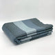 Toacazo baby alpaca wool blanket – a folded, multicolored blanket with gray, blue, and dark green stripes rests neatly on a smooth, plain white surface