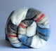 Siguitag alpaca wool throw blanket – a multicolored, striped woolen blanket is tightly rolled up. It features shades of gray, red, blue, and cream against a plain, light background