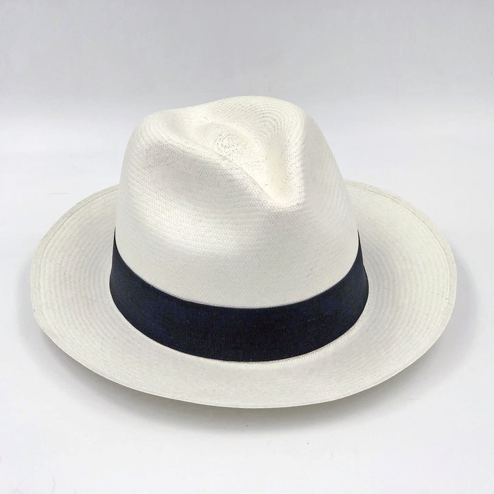 A white Panama hat with a black band sits upright on a plain white surface, showcasing its woven texture and classic style.