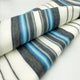 Teinza baby alpaca wool blanket – a folded, striped fabric features alternating bands of gray, blue, and white, resting on a smooth light surface
