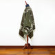 Clint Eastwood alpaca wool poncho – a brown poncho with white geometric patterns drapes over a wooden mannequin stand, set against a plain white wall and wooden floor