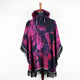 Hooded poncho hangs on a mannequin, displaying a vibrant purple and black tie-dye pattern with fringe edges and striped trim, set against a plain white background.