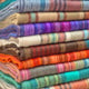 Wholesale lot of 10 queen alpaca wool blankets – colorful, striped woolen blankets are stacked neatly, showcasing a variety of vibrant patterns and textures. The context suggests a textile shop or craft display focusing on warm fabrics