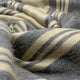 Chalua baby alpaca wool blanket – a soft, woolen fabric with black and cream stripes is laid out, creating gentle folds and a cozy texture, suggesting warmth and comfort