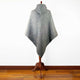 A gray hooded poncho is displayed on a wooden stand, set against a plain white background and a hardwood floor.