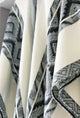 A wool blanket drapes gently, showcasing a geometric black and white pattern. It hangs against a light, neutral wall, creating an elegant and cozy atmosphere.