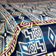 Geometric-patterned fabric, featuring multicolored designs including diamonds and lines, draped smoothly across a flat surface. The fabric's intricate patterns create a vibrant, visually textured appearance.