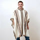 A person wears a cream poncho with geometric brown and black patterns, standing against a plain, light background.