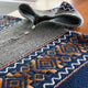 A knitted sweater, featuring geometric patterns in blue, brown, and white, is laid on a wooden surface. The collar is unbuttoned, revealing textured gray fabric.