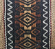 The textile features intricate geometric patterns in shades of brown and black, interwoven with white zigzag accents, set in a richly textured fabric, suggesting traditional craftsmanship.