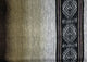 A woven textile displays gradient stripes from dark to light gray, with an intricate geometric pattern on the right edge, featuring diamond shapes in black and white.