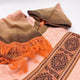 The poncho features a brown and orange gradient hood with a button, orange fringe, and geometric patterns, lying on a light surface.