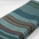 Pallalanga baby alpaca wool blanket – a folded woolen blanket features horizontal stripes in shades of green, blue, brown, and red, lying on a flat, white surface