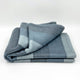 Toacazo baby alpaca wool blanket – a folded, soft, blue and gray blanket lies neatly on a plain white surface, displaying its subtle geometric pattern in varying shades