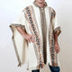 A person wears a cream wool poncho with brown geometric patterns, standing with one hand on the hip. The context is a plain white background.