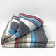 Carihuairazo baby alpaca wool blanket – folded, multi-colored striped blanket with shades of blue, red, gray, and white lie on a plain white background