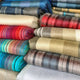 Wholesale lot of 10 queen alpaca wool blankets – stacks of colorful, folded blankets are arranged neatly. The blankets feature various striped patterns and vibrant colors, creating a warm and inviting display in an indoor setting
