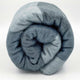 Toacazo baby alpaca wool blanket – a thick, soft blanket is tightly rolled, displaying a blend of gray and white colors, set against a plain white background