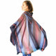 A woman wearing a colorful, striped shawl poses with her back slightly turned. The setting is minimal, with a plain white background emphasizing the shawl's patterns.