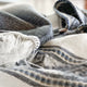 Palora lightweight alpaca wool hooded poncho – a folded, fringed gray and white woolen poncho rests on a surface, featuring striped patterns and a button, suggesting warmth and cozy domesticity in a softly lit setting